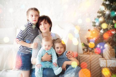 Üç kızı olan bir anne Noel ağacının yanında yerde oturuyor.