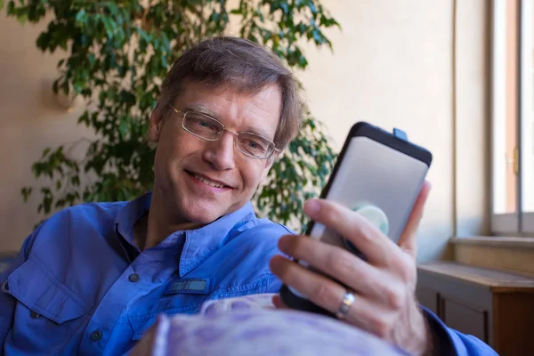 Caucasian Man Forties Blue Shirt Sitting Sofa Smiling Looking Smartphone — Stock Photo, Image