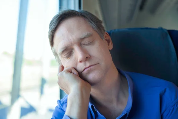 Белый мужчина в синей рубашке спит у окна поезда — стоковое фото