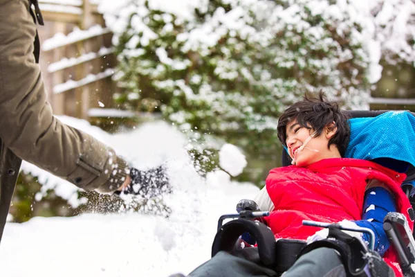 Мальчик-инвалид в инвалидной коляске играет в зимний снег — стоковое фото