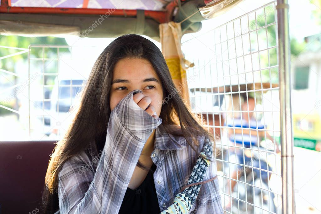 Teen girl riding tuktuk in Cambodia, covering nose from pollutio