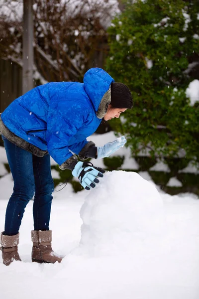 Teen girl wearing  winter clothing outside building snowman in y — Stock Photo, Image