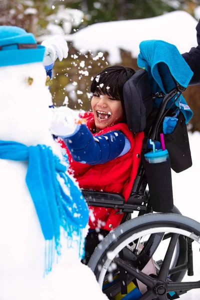 Счастливый улыбающийся мальчик-инвалид в инвалидной коляске строит снеговика — стоковое фото