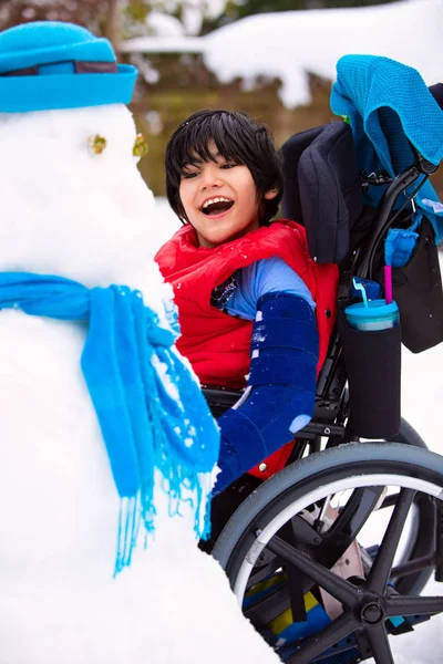 Szczęśliwy uśmiechający się wyłączone chłopak na wózku inwalidzkim, budowa snowman — Zdjęcie stockowe
