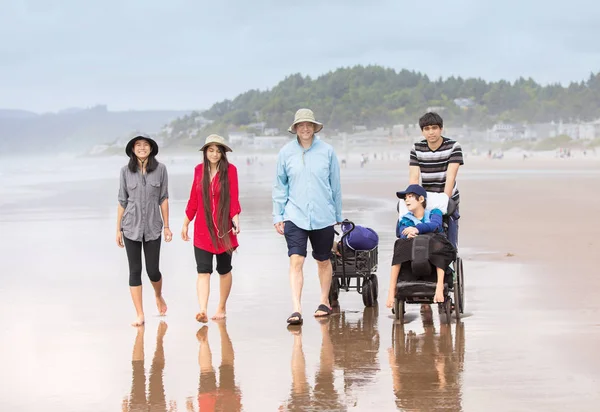 Мультирасовая семейная прогулка по пляжу с сыном-инвалидом на колесах — стоковое фото