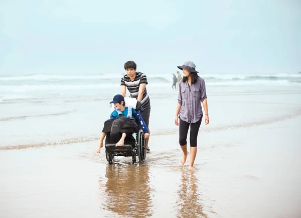 Geschwister gehen behinderten Bruder im Rollstuhl im Wasser entlang b — Stockfoto