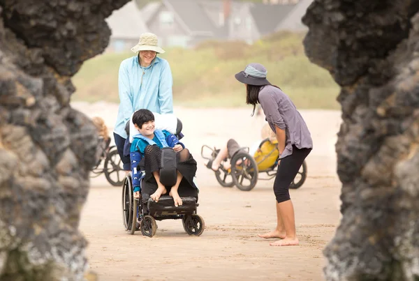 Padre e figlio disabile in sedia a rotelle sulla spiaggia con la famiglia — Foto Stock