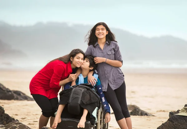 Hermano discapacitado en silla de ruedas dando mayor hermana beso en la playa — Foto de Stock