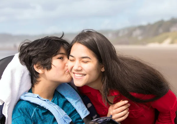 Мальчик-инвалид в инвалидной коляске на пляже целует сестру — стоковое фото