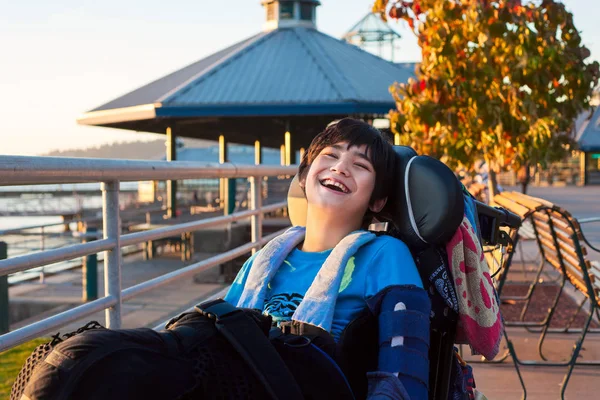 Мальчик-инвалид в инвалидной коляске в парке, улыбается на открытом воздухе — стоковое фото
