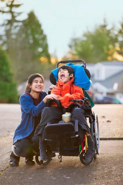 Zus naast een handicap kleine broertje in de rolstoel buitenshuis — Stockfoto