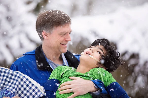 Ojciec trzyma niepełnosprawnego syna na zewnątrz podczas opadów śniegu — Zdjęcie stockowe