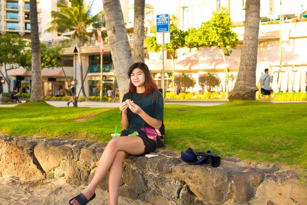 出生アジアの白人10代の少女観光客リラックスし ワイキキ ホノルル ハワイの石の壁に座ってKuhuiビーチでハムMusbiを食べる — ストック写真