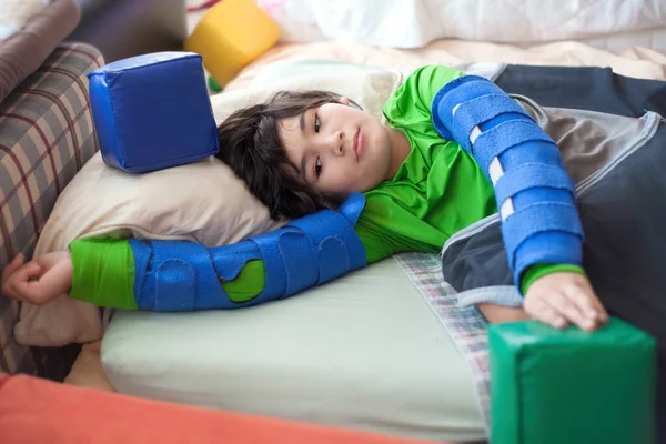 漂亮的出生残疾小男孩躺在床垫上玩泡沫块 同时还戴着臂膀 — 图库照片