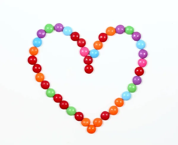 Sweet heart made from colored smarties. Chocolate candies in a shape of heart on white background, top view.