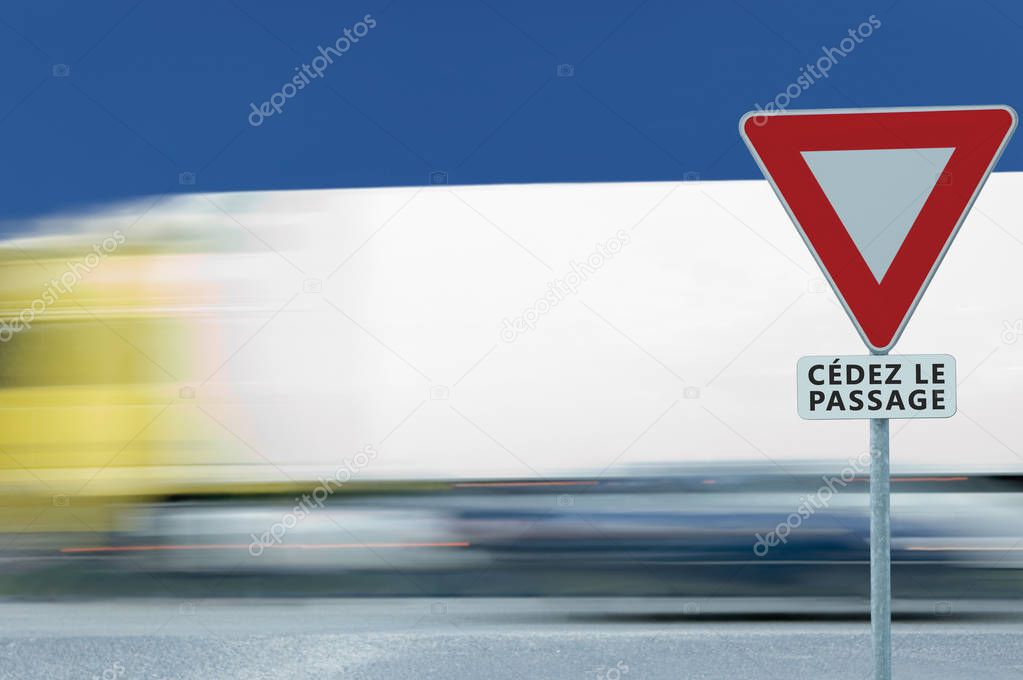Give way yield french cedez le passage road sign, motion blurred truck vehicle traffic background, white signage triangle red frame regulatory warning, metallic pole post, blue summer sky, panneau signalisation cedez-le-passage, France