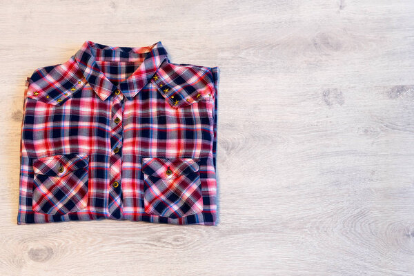 Multi-colored checkered women's shirt lying neatly folded on a light wooden background