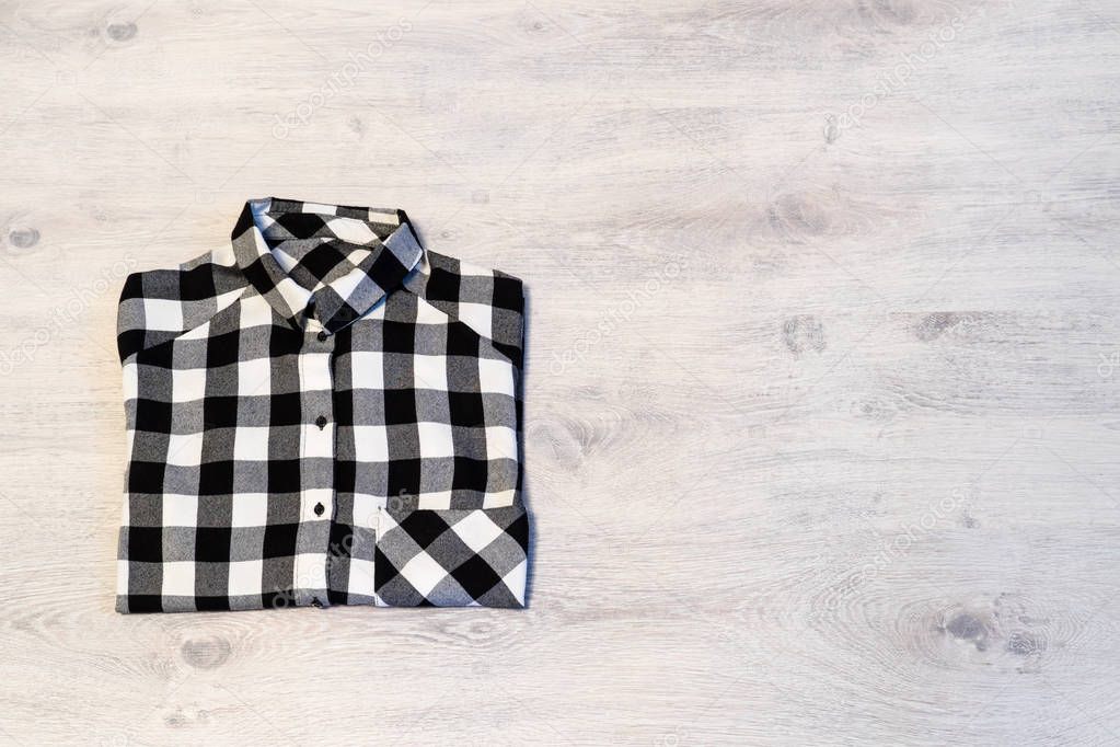 Multi-colored checkered women's shirt lying neatly folded on a light wooden background