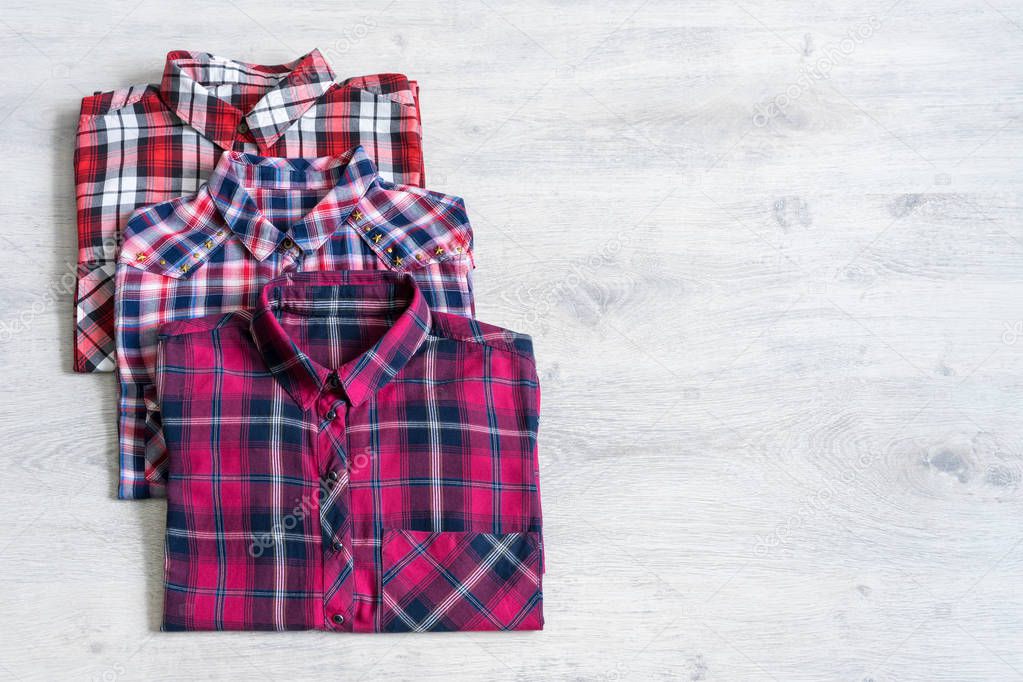 Three multi-colored checkered women's shirts lying neatly folded on a light wooden background