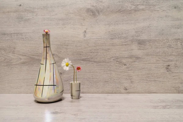 Summer creative still life in minimal style. White and pink Marguerite daisy flowers in vintage pearl flagon and in small liqueur glass on light grey background