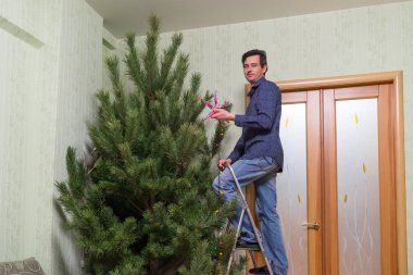 Yakışıklı orta yaşlı adam bir yıldız ve salon iç merdiven üzerinde duran renkli ampuller çelenk ile Noel ağacı süsle. Yeni yıl tatil kavramı, rahat ev