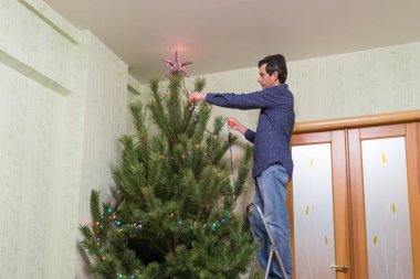 Yakışıklı orta yaşlı adam bir yıldız ve salon iç merdiven üzerinde duran renkli ampuller çelenk ile Noel ağacı süsle. Yeni yıl tatil kavramı, rahat ev