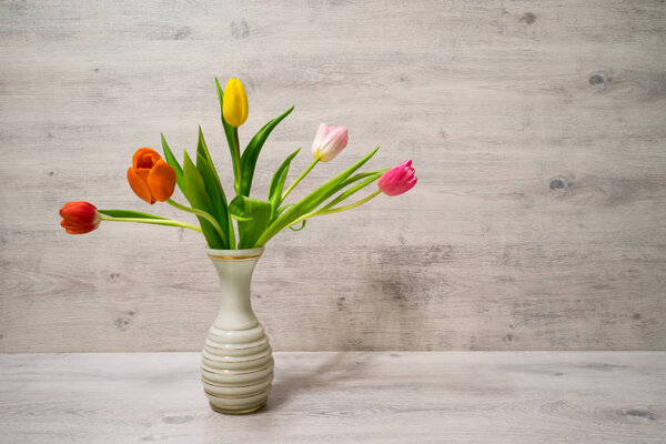 Colorful spring bouquet of tulip flowers in a vase on wooden background