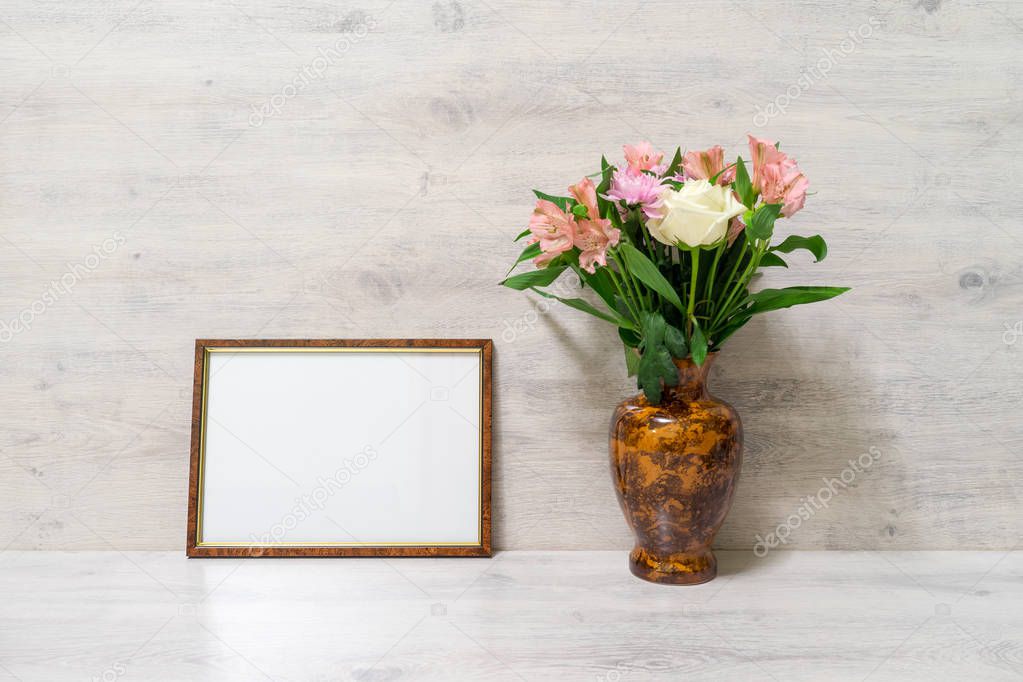 Colorful spring bouquet of rose, chrysanthemum and alstroemeria flowers in a vase with empty photoframe on wooden background