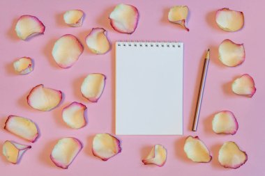 Defter ve kalem pembe pastel Kağıt arka plan üzerinde kurutulmuş krem gül yaprakları ile. Aşk ve romantizm kavramı, alay etmek yukarıya. Yat, uzay, üstten görünüm Kopyala