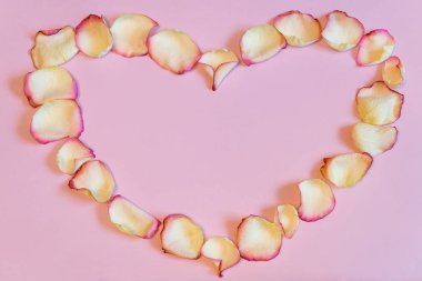 Çerçeve pembe pastel Kağıt arka plan üzerinde kalp şeklinde kurutulmuş krem gül yaprakları. Aşk, romantizm ya da Sevgililer günü kavramı, alay etmek yukarıya. Yat, uzay, üstten görünüm Kopyala