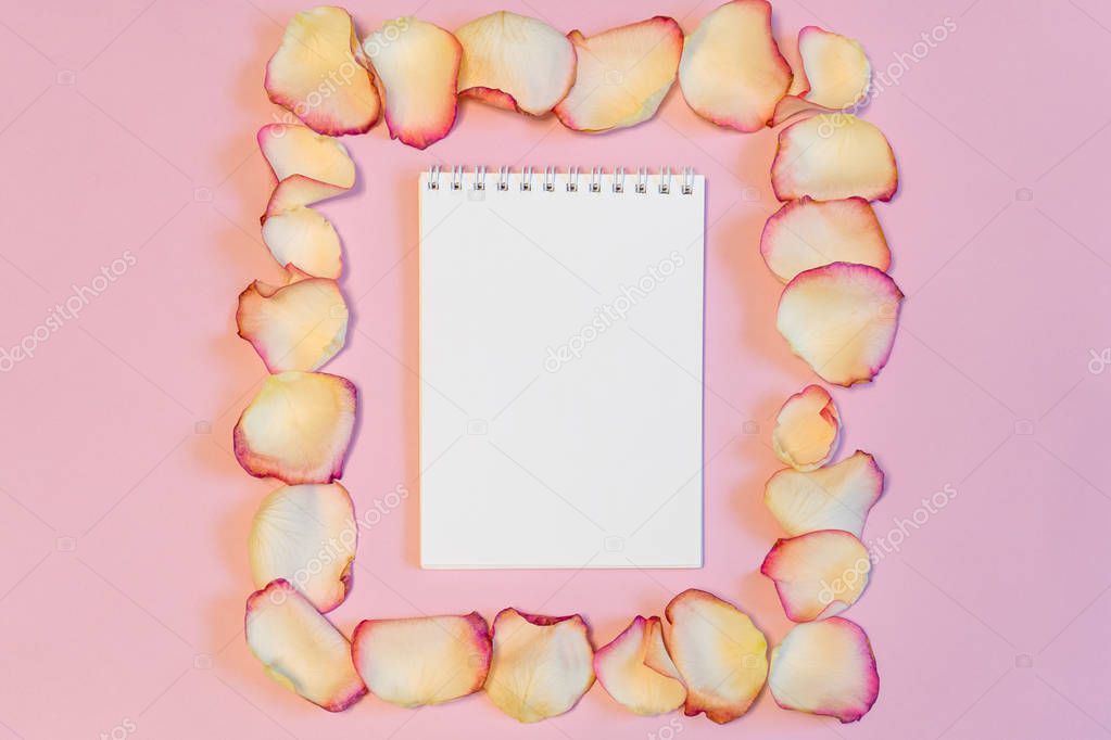 Notebook in frame of dried cream rose petals on pink pastel paper background. Love or romance concept, mock up. Flat lay, copy space, top view
