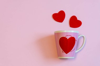Kupa kahve veya çay ve pastel pembe üzerinde iki kırmızı kalp. Yaratıcı düzeni en az tarzı. Aşk, romantizm ya da Sevgililer günü kavramı