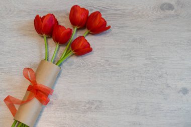 Kraft kağıt hafif ahşap arka plan üzerinde kırmızı fiyonklu kırmızı lale. Güzel bahar çiçek düzeni. Kadın ya da anne için tebrik kartı gün. Düz yatıyordu, en iyi görünüm, kopya alanı