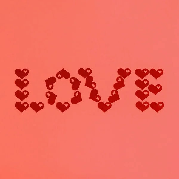 Text LOVE made of red confetti hearts on living coral background. Love, romance or Valentine\'s day concept. Color of the year 2019