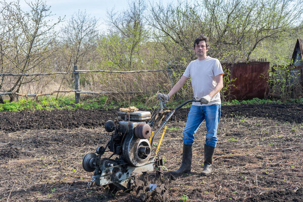 Man with cultivator ploughs ground. Land cultivation, soil tillage. Spring work in the garden. Gardening concept.