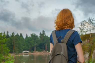 Genç güzel Bayan sırt çantası açık havada yaz akşamları yürüyüş ile. Güzel manzara arka plan üzerinde turist. Monrepos Park, Vyborg, Rusya Federasyonu. Seyahat kavramı