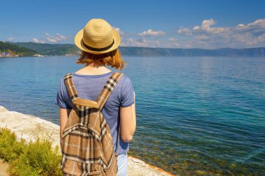 Ara yayılma turist kız şapka ve güneşli yaz günde waterfront Listvyanka Köyü üzerinden Deniz Baykal güzel manzara hayran sırt çantası. Seyahat, özgürlük ve yaz tatil kavramı