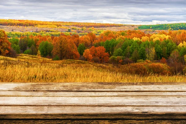 Κενό ξύλινο τραπέζι με θολή γραφικό φθινοπωρινό τοπίο πανοραμική θέα από λόφο σε πεδινό με πεδίο και άλσος σε συννεφιασμένη μέρα. Προσομοίωση για προϊόντα εμφάνισης ή μοντάζ — Φωτογραφία Αρχείου