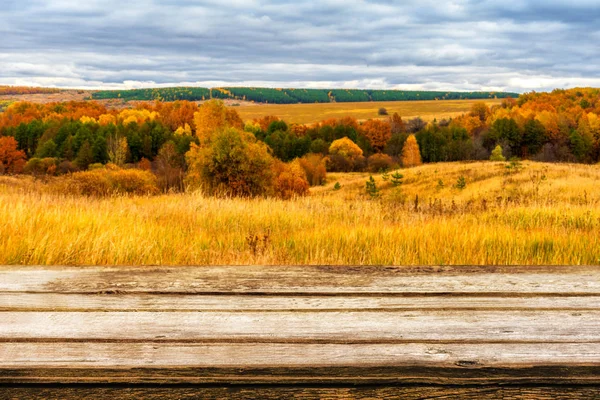 Mesa de madera vacía con un pintoresco paisaje otoñal borroso de vista panorámica desde la colina hasta las tierras bajas con campo y arboleda en un día nublado. Maquillaje para productos de exhibición o montaje — Foto de Stock