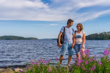 Turistler yaz güneşli günlerinde güzel manzaralara karşı poz veren orta yaşlı erkek ve kadın. Ladoga Gölü kıyısında ayakta duran bir çift. Dünya 'nın uzak yerlerini gezmek ve keşfetmek. Karelia, Rusya