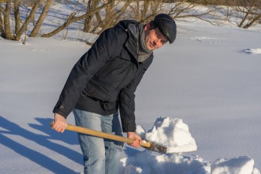 Güneşli bir günde ev sahasında kar temizleyen yakışıklı orta yaşlı beyaz bir adam. Kır evinden yola kürek döşeyen bir adam. Kış aktif eğlence kavramı