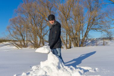 Güneşli bir günde ev sahasında kar temizleyen yakışıklı orta yaşlı beyaz bir adam. Kır evinden yola kürek döşeyen bir adam. Kış aktif eğlence kavramı