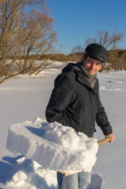 Güneşli bir günde ev sahasında kar temizleyen yakışıklı orta yaşlı beyaz bir adam. Kır evinden yola kürek döşeyen bir adam. Kış aktif eğlence kavramı