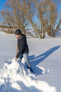 Güneşli bir günde ev sahasında kar temizleyen yakışıklı orta yaşlı beyaz bir adam. Kır evinden yola kürek döşeyen bir adam. Kış aktif eğlence kavramı