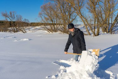 Güneşli bir günde ev sahasında kar temizleyen yakışıklı orta yaşlı beyaz bir adam. Kır evinden yola kürek döşeyen bir adam. Kış aktif eğlence kavramı