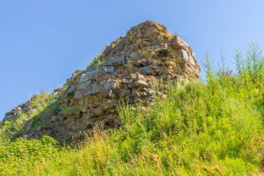 Antik mimari gösteriler, güneşli bir yaz gününde mavi gökyüzüne karşı yeşil çimlerle kaplanmış harabeler oluşturuyor. Seyahat, turizm veya tarih temaları için arka plan.