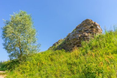 Antik mimari gösteriler, güneşli bir yaz gününde mavi gökyüzüne karşı yeşil çimlerle kaplanmış harabeler oluşturuyor. Seyahat, turizm veya tarih temaları için arka plan.