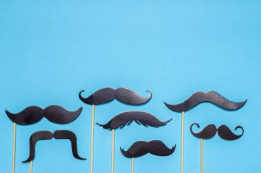 Çeşitli siyah fotoğraf kulübeleri mavi arka planda farklı şekildeki bıyıkları destekliyor. Babalar Günü için tebrik kartı ya da erkek sağlığı bilinçlendirme kampanyası konsepti. Düz konum, metin için boşluk, maket.