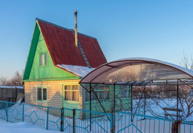 Boş banliyö arazisi karla kaplanmış ve kış akşamında kış tuğlalı kulübe için gün batımına doğru yola çıkmış. Rus konsepti.