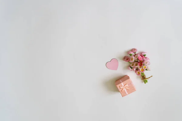 Composición creativa de verano en estilo minimalista. Ramo de flores de Margarita blanca y rosa con corazón y caja de regalo sobre fondo blanco. Vista superior, plano, espacio para copiar - foto de stock